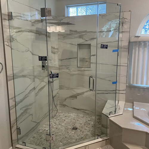 Shower enclosure withstone tiles and marble and glass doors by Dunn's Flooring Depot