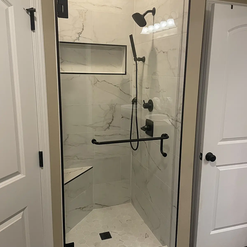 Shower enclosure with marble tiles and glass doors by Dunn's Flooring Depot